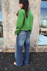 Chaqueta corta de tejido efecto ante en color verde vibrante, con cuello solapa, cierre frontal de cremallera y mangas largas. Presenta dos bolsillos frontales con solapa decorados con arandelas metálicas en el pecho.