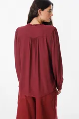 Camisa de manga larga color azul, con cuello mao y detalle de volados en la botonadura frontal. Presenta puños abotonados y un corte recto y fluido.