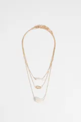 Collar triple de cadena fina dorada con tres dijes distintos: un cilindro de resina, un aro irregular y una piedra ovalada.