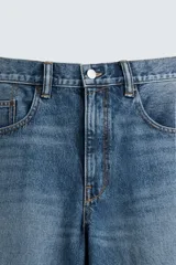 Bermuda de denim de algodón, color azul medio lavado, de corte ancho (baggy fit) y largo hasta la rodilla. Presenta cinco bolsillos y cierre frontal con cremallera y botón.