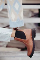 Bota tipo Chelsea de cuero color suela, con paneles laterales elásticos en color negro y suela robusta dentada de goma negra.