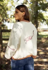 Buzo de algodón color crema con cuello redondo, puños y ruedo en color tostado. Presenta una línea horizontal marrón y el texto 'azu' bordado en color rosado en el pecho.