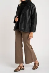 Chaqueta tipo gamulán de color negro con forro de corderito sintético al tono. Presenta solapas anchas, cierre frontal con botones y un diseño entallado al cuerpo.