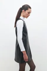 Minivestido negro de cuero ecológico con cuello redondo y sin mangas. Presenta tachas plateadas en el frente y cierre trasero.