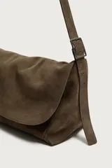 Bandolera de piel con acabado en serraje, color marrón, con compartimento principal con cierre de solapa y cremallera, bolsillos interiores y asa de hombro ajustable.
