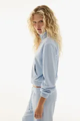 Campera corta de velour color celeste claro, con cuello elevado, cierre frontal y bolsillos insertados. Presenta elástico fruncido en puños y bajo.