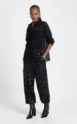 Pantalon de corte recto y holgado, confeccionado en tejido cubierto de lentejuelas negras. Presenta una cinturilla elástica ancha en contraste, bolsillos laterales con cierre y diseño de tiro alto.