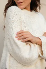 Buzo tejido de punto con cuello redondo, manga larga y diseño holgado. Presenta tajos laterales y un corte asimétrico, siendo ligeramente más largo en la parte posterior.