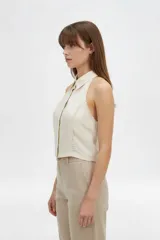 Top halter color beige, confeccionado en viscosa, de corte al cuerpo y sin mangas, con cierre frontal de botones y detalles de costuras decorativas.