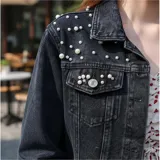 Campera de jean color negro con apliques de perlas en la parte superior frontal. Presenta cuello clásico, cierre frontal con botones metálicos y dos bolsillos en el pecho.