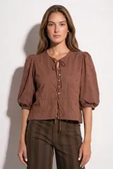 Blusa blanca de algodón con delicado bordado floral, mangas abullonadas de largo 3/4 y cierre frontal con botones y cordón ajustable en la cintura.