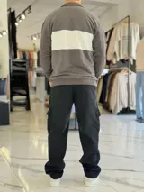 Hoodie de corte clásico con medio cierre y cuello alto, en color marrón con una franja horizontal blanca en el pecho que incluye el logo estampado en negro. Presenta además un pequeño bordado en el hombro izquierdo y puños y cintura elastizados de rib.