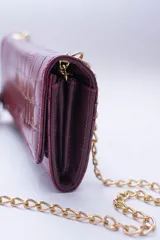 Cartera tipo sobre color beige con textura granulada y correa de cadena dorada.