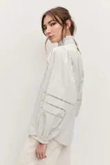 Camisa de manga larga color marrón, con cuello alto con volados, botonadura frontal y detalles calados en las mangas abullonadas.