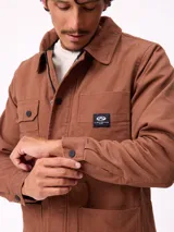 Sobrecamisa de algodón color marrón, con cierre frontal de cremallera y botones a presión. Presenta cuello clásico, dos bolsillos frontales con solapa y cierre de botón, y forro interior de poliéster.