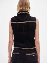 Chaleco de pana negro con cierre frontal de botones metálicos dorados. Presenta detalles de costuras en contraste en el cuello, cartera y canesú, e incluye un pequeño parche con forma de bandera en el pecho.