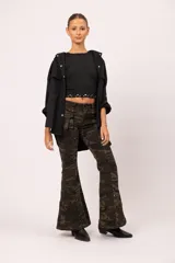 Pantalón de jean con estampado camuflado en tonos verdes y marrones, de corte oxford con bota ancha. Presenta bolsillos tipo cargo laterales, detalles de tachas metálicas en la cintura y bolsillos, y cierre frontal con botón.