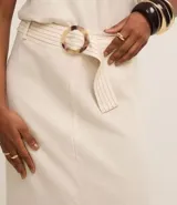 Pollera midi color blanco hueso, de corte recto con tajo frontal. Confeccionada en viscolino, presenta un cinturón con hebilla redonda y detalles de pespuntes y encaje en la parte delantera.