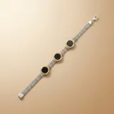 Pulsera de malla tejida en plata, con tres dijes circulares de ónix negro enmarcados en oro amarillo con detalles estriados.