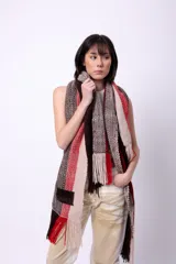 Bufanda de lana merino tejida en telar, con diseño de rayas en tonos marrón, beige y rojo. Presenta flecos en los extremos y un parche negro con la palabra "CAPER" en blanco.