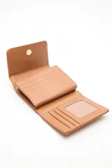 Billetera compacta de cuero sintético negro, con solapa que combina texturas lisas y efecto reptil. Incluye un aplique metálico circular con logo grabado en el frente y cierre con broche.