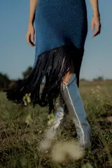 Vestido tejido en lurex color plateado, con diseño geométrico en cuero en el frente y flecos en el ruedo. Breteles finos de cuero con tientos plateados.