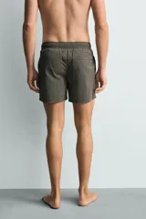 Bañador de hombre de largo medio, color celeste claro con rayas blancas horizontales. Presenta cintura elástica ajustable con cordón, bolsillos frontales y bolsillos traseros de plastrón. Incluye forro interior.