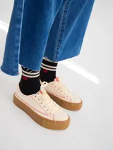 Championes bajos color crema con pespuntes rojos, capellada de tela canvas y plataforma de goma color caramelo de 4 cm de altura.