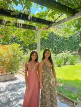 Vestido largo con escote en V, estampado en tonos rojizos y rosados, con un patrón ondulado. Presenta cut-outs laterales bajo el busto y breteles finos que se cruzan en la espalda.