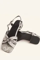 Sandalias bajas con estampado de piel de serpiente en tonos blanco y negro. Tiras finas entrecruzadas en el empeine, pulsera al tobillo con hebilla ajustable y pequeño tacón cuadrado.