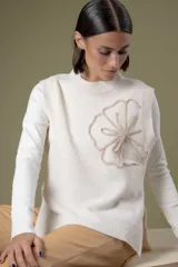 Chaleco de lana color crema con diseño de flor bordada en relieve en el frente, cuello redondo y aberturas laterales en el ruedo.