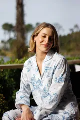 Pijama de algodón con estampado toile de jouy en azul sobre fondo blanco, compuesto por una camisa de manga larga con cuello solapa y botones frontales, y un pantalón recto con cintura elástica.