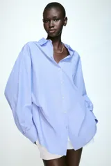 Camisa de manga larga en tejido de popelín color celeste, con cuello solapa, cierre frontal con botones y detalle de pliegue en el bajo.