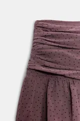 Falda pantalón de tiro medio en color bordó con estampado de lunares pequeños. Presenta un diseño con volantes escalonados y un detalle asimétrico lateral con caída fluida.