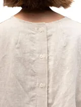 Remera de lino con corte holgado, cuello redondo y mangas cortas. Presenta un diseño minimalista con detalle de botones en la espalda.