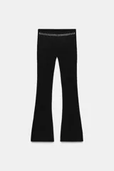 Pantalon negro de corte flare, confeccionado en tejido elastizado. Presenta tiro alto, cintura elastizada y detalle de tachas metálicas decorativas en la parte superior.
