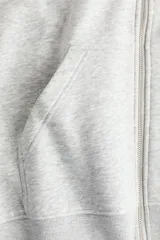 Campera canguro de felpa color gris melange, de corte holgado con interior cepillado suave. Cuenta con hombros caídos, capucha forrada, cierre frontal y bolsillos delanteros abiertos, con puños y bajo en punto acanalado.