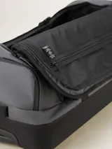 Valija gris con ruedas, manija extensible y correas de ajuste externas.