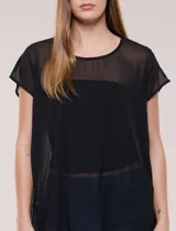 Blusa larga negra de gasa liviana con silueta amplia y desestructurada, escote redondo, mangas cortas caídas y bajo asimétrico más largo en la parte posterior.