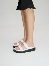 Sandalias de cuero vacuno color marrón con acabado brillante, diseño de dos tiras anchas acolchadas y plataforma baja.
