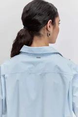 Camisa de algodón color celeste claro, con cuello clásico, cierre frontal de botones y detalle de tachas metálicas plateadas distribuidas por toda la prenda.