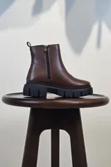 Bota de caña corta color marrón, con cierre lateral y suela track negra de goma con plataforma.