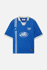 Camiseta tipo polo de fútbol Scuffers color azul, de corte boxy fit, confeccionada en tejido microperforado. Presenta cuello y puños en color crudo, franjas verticales blancas en el lado derecho y estampados tipográficos en el pecho.