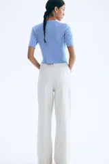 Cárdigan corto de punto acanalado en color celeste, con cuello redondo, manga corta y cierre frontal de botones dorados. Presenta dos bolsillos delanteros decorativos con botón dorado.