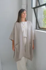 Poncho abierto de tejido de punto en color visón, con diseño holgado, mangas cortas y bolsillos frontales aplicados.