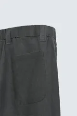 Pantalón de corte relajado confeccionado en tejido de cáñamo color blanco roto. Presenta cintura elástica con cordón interior ajustable, cierre frontal con botones, bolsillos laterales y un bolsillo trasero de plastrón.