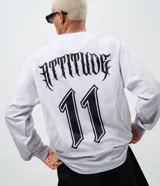 Remera de manga larga estilo deportivo con corte boxy, confeccionada en poliéster. Presenta cuello redondo, paneles laterales en tejido texturizado y estampados gráficos estilo tribal y lettering gótico en el frente.