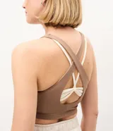 Top deportivo de microfibra marca Get Over, de diseño bicolor en tonos marrón y marfil, con escote redondo, capas superpuestas, breteles anchos cruzados y abertura en la espalda.