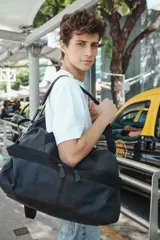 Bolso de mano tipo duffle de cuero negro, con doble asa corta y correa larga regulable con el logo de la marca. Tiene cierre superior y dos bolsillos frontales con cierre.