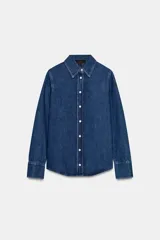 Camisa de denim azul oscuro con cuello solapa, manga larga con puños anchos y bajo asimétrico. Cierre frontal con botones blancos.